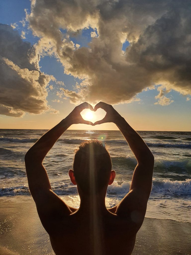peaceful and meditional view on a sunset at the beach with two hands forming a heart